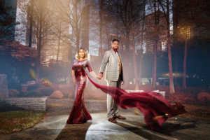 Houston couple in elegant wedding attire holding hands with the bride’s long burgundy train flowing in the breeze in an urban park setting.